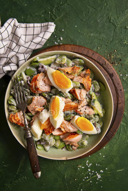 Ensalada con habas, pepino, aceitunas, salmón, huevo y aderezo de yogur griego - foto de stock