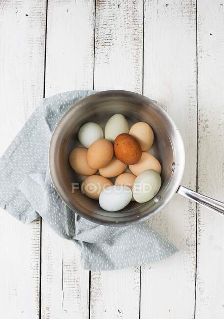 White and brown eggs in metal pot with blue cloth — Stock Photo