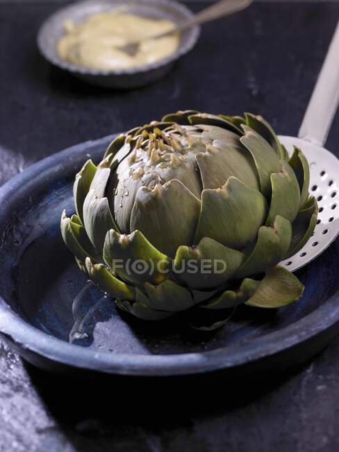 A boiled artichoke on a slotted spoon — Stock Photo