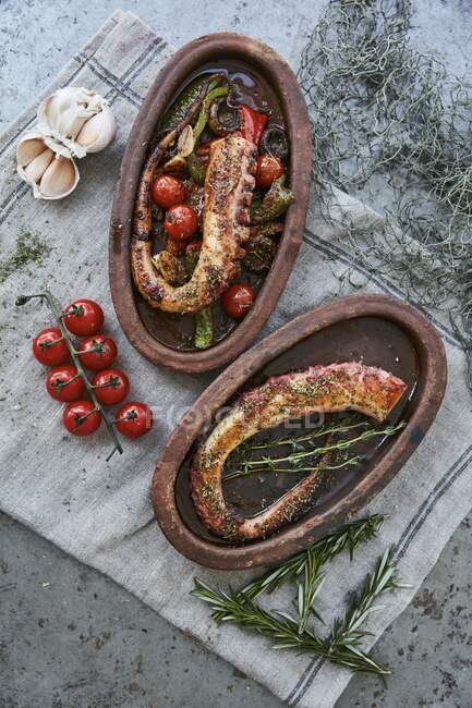 Octopus tentacles with tomatoes, peppers and herbs in rustic serving dishes — Stock Photo