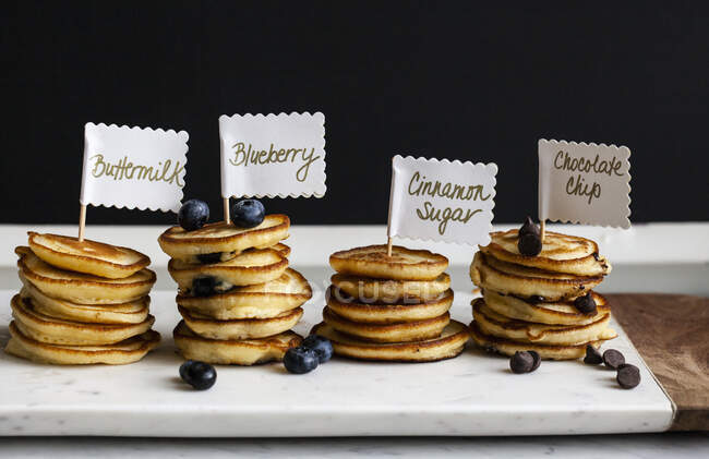Stapelweise Mini-Pfannkuchen mit Schildern, Obst und Schokoladenstücken auf einem Marmorbrett — Stockfoto