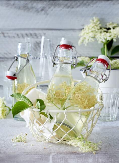 Elderflower syrup in small bottles in a wire basket — Stock Photo