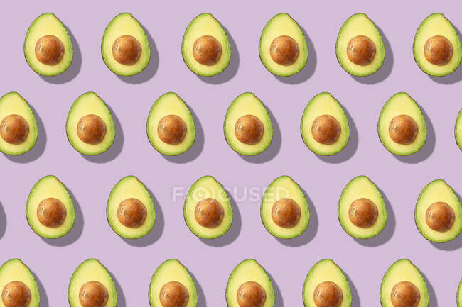Lots of halved avocados in rows on a purple surface — Stock Photo