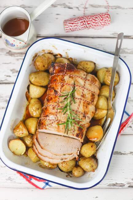 Roasted pork tied with string and potatoes in tin — Stock Photo