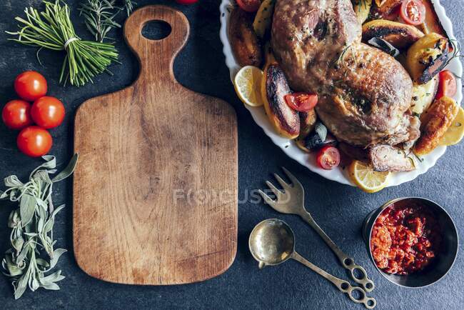 Ein leeres Holzbrett mit Putenbein, Gemüse und Ajvar-Relish daneben — Stockfoto