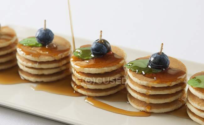 Several piles of mini pancakes with maple syrup, blueberries and mint — Stock Photo