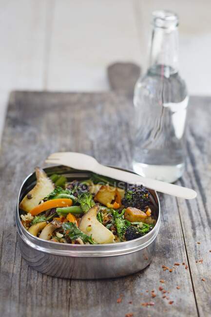 Lentilles et riz aux champignons, carottes et brocoli dans une boîte à lunch devant une bouteille d'eau — Photo de stock