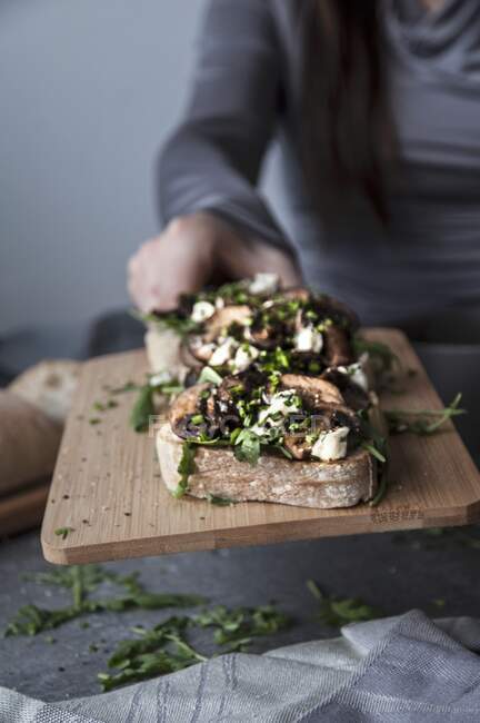 Bruschetta with mushrooms, feta and rocket on a wooden chopping board — Stock Photo