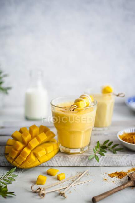Lássi de mango con cúrcuma y miel, mango fresco en un lado - foto de stock