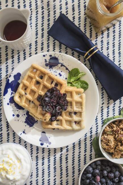 Blueberry Lemon Waffles shot from overhead on table styled with sptriped tablecloth and navy rolled napkin — Stock Photo