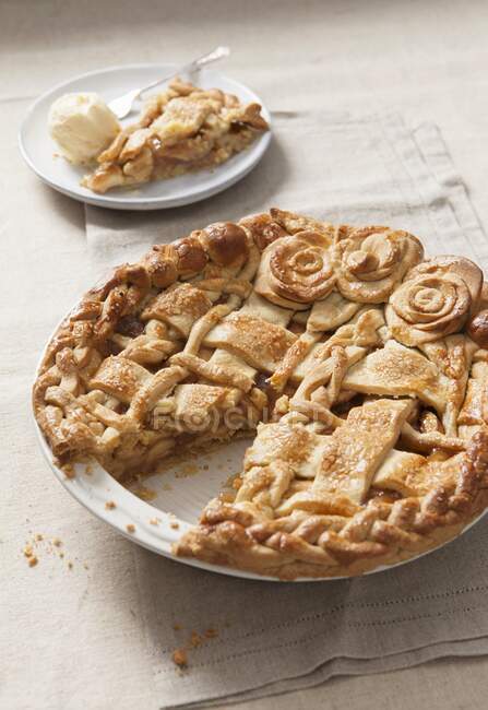 Apple pie with dough lattice and pastry roses in baking dish, cut portion on background — Stock Photo