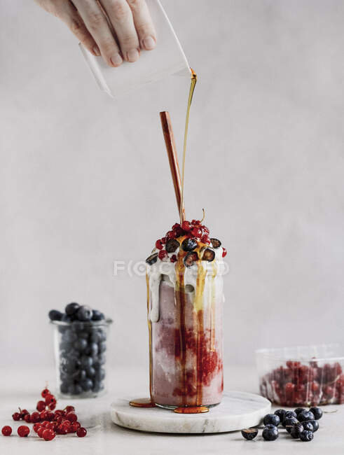 Mão derramando xarope de bordo em Fruit milkshake em vidro — Fotografia de Stock
