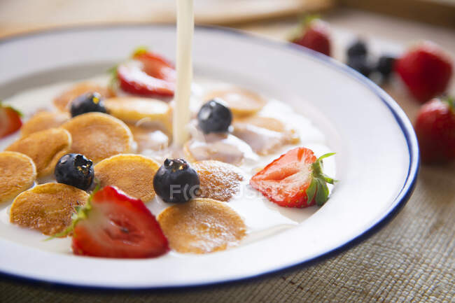 Мини-блины в миске с молоком и фруктами — стоковое фото