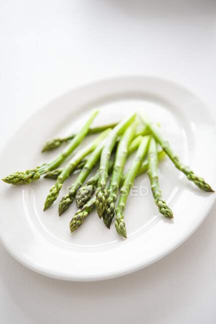 Uncooked green asparagus on a white serving platter — Stock Photo
