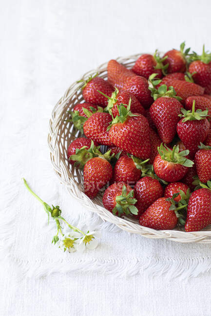 Erdbeeren im Korb mit Blumen auf weißer Tischdecke — Stockfoto