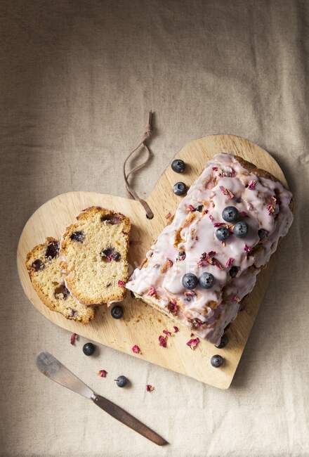 A sliced blueberry loaf cake with icing and dried rose petals — Stock Photo