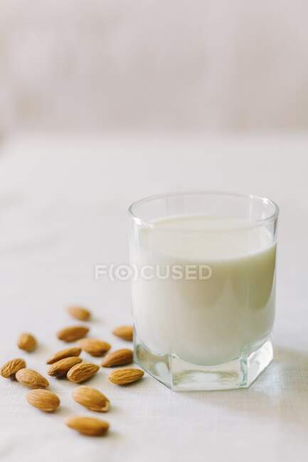 Un vaso de leche y almendras sobre un mantel blanco - foto de stock