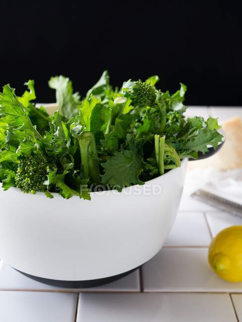 Broccolini in einer weißen Schüssel, daneben eine Zitrone und ein Block Parmesan — Stockfoto