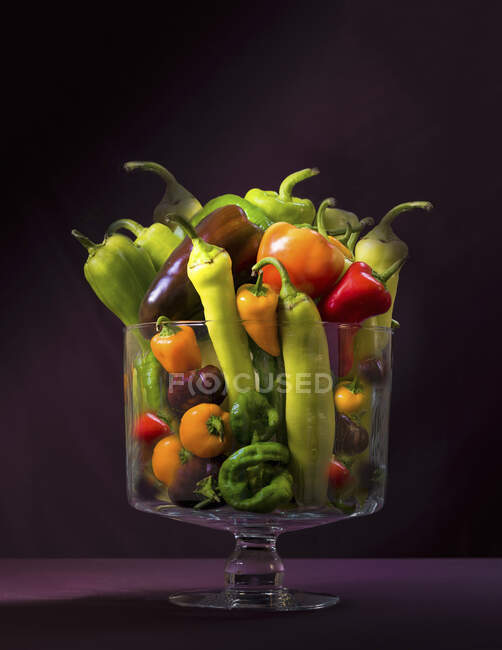 Différents types de poivrons dans un bocal en verre sur un fond sombre — Photo de stock