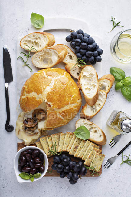 Запечённый бри, завернутый в слоеное тесто с грибами с хлебом и крекером на доске — стоковое фото