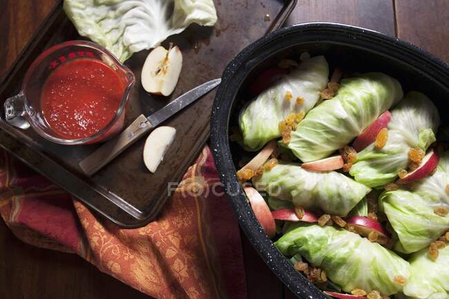Stuffed cabbage in roasting pan with apple slices, rasins and tomato sauce — Stock Photo
