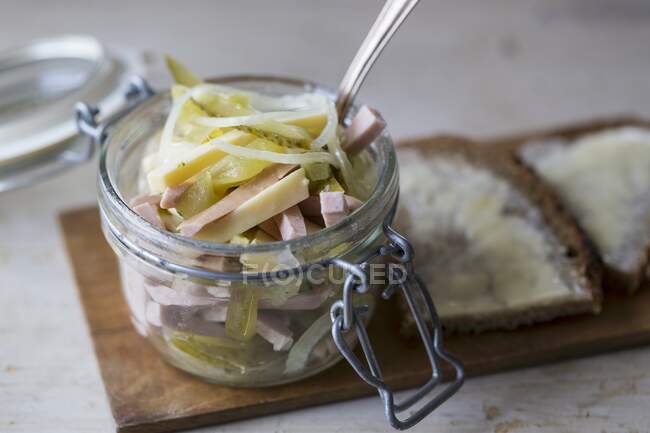 Swiss sausage salad in a glass jar with buttered bread — Stock Photo