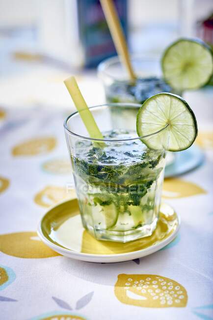 Mojito with lime slice and straw in glass on small saucer — Stock Photo