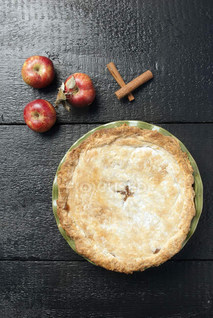 Apple pie with apples and cinnamon on wooden surface — Stock Photo