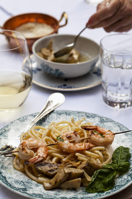 An outdoor table with pasta cacio e pepe (pasta with cheese and pepper), shrimp skewers with basil, artichokes and white wine — Stock Photo