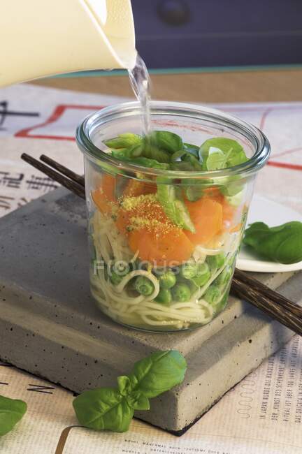 Hacer sopa de fideos asiáticos en un vaso: Añadir agua caliente y dejar cocer - foto de stock