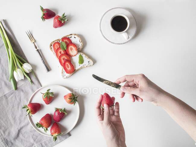 Eine Hand schneidet Erdbeeren für ein offenes Sandwich (von oben gesehen)) — Stockfoto