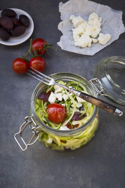 Zucchini noodles in glass jar with tomatoes, feta and olives — Stock Photo
