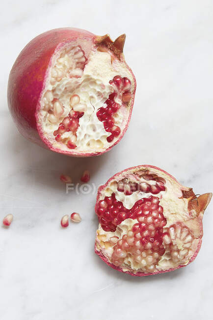 Pomegranate whole and in pieces with scattered seeds on a dark background — Stock Photo