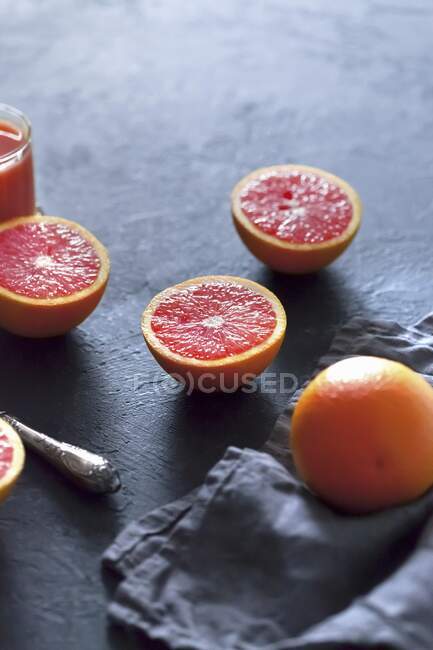 Naranjas de sangre, enteras y cortadas a la mitad, sobre una superficie gris de hormigón - foto de stock