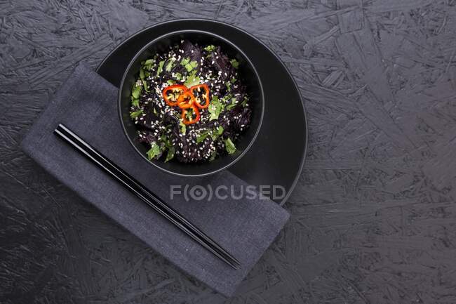 Un tazón de arroz negro con setas miso rematado con cilantro picado, semillas de sésamo y chile rojo. Servido en un tazón negro - foto de stock