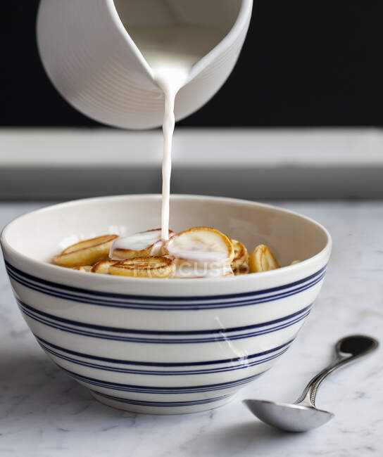 Latte versato su una ciotola blu e bianca di mini pancake cereali — Foto stock