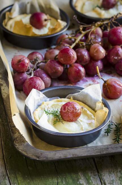 Mini goat's cheese tarts with purple grapes in baking tins — Stock Photo