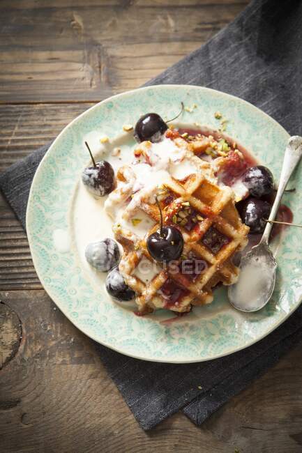 Round Belgian waffles with cream, cherries and chopped pistachios — Stock Photo