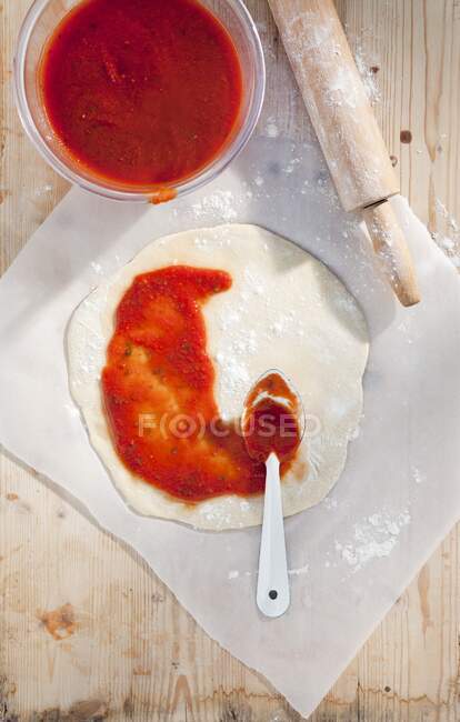 Томатный соус на развернутом тесте для пиццы — стоковое фото