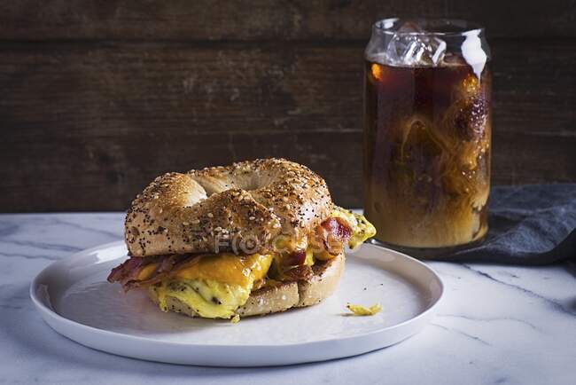 Bacon, scrambled egg and cheese bagel served with glass of ice tea — Stock Photo