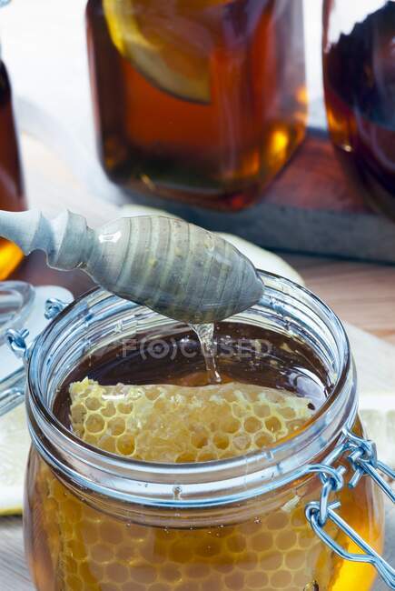 Un frasco de vidrio de miel orgánica con panal y una cuchara de miel - foto de stock