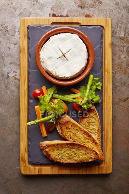 Baked cheese with toasted bread and vegetables on board — Stock Photo