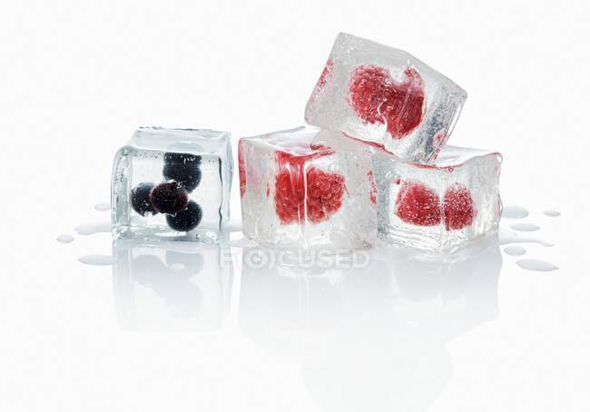 Cubos de hielo con arándanos y frambuesas sobre fondo blanco con reflejo - foto de stock