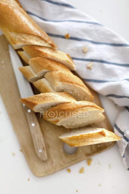 Baguete, cortada em fatias, numa tábua de madeira — Fotografia de Stock