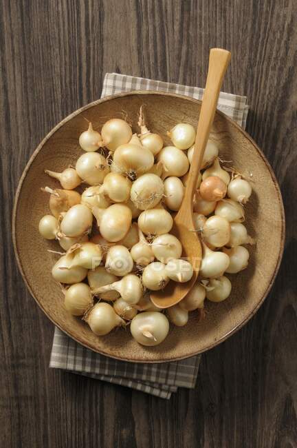 Onions with a wooden spoon on a wooden plate (top view) — Stock Photo