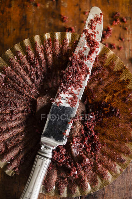 The remains of a chocolate muffin in a paper case with a knife — Stock Photo