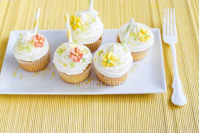Frühlings-Cupcakes mit Zuckerblumen auf Teller und Gabel auf gelbem Tisch — Stockfoto