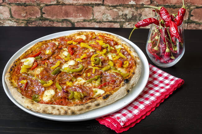 Pizza a base di pasta madre, salsa di pomodoro con origano e olio d'oliva, mozzarella, peperoni verdi, gialli e rossi, salame piccante e salame piccante — Foto stock