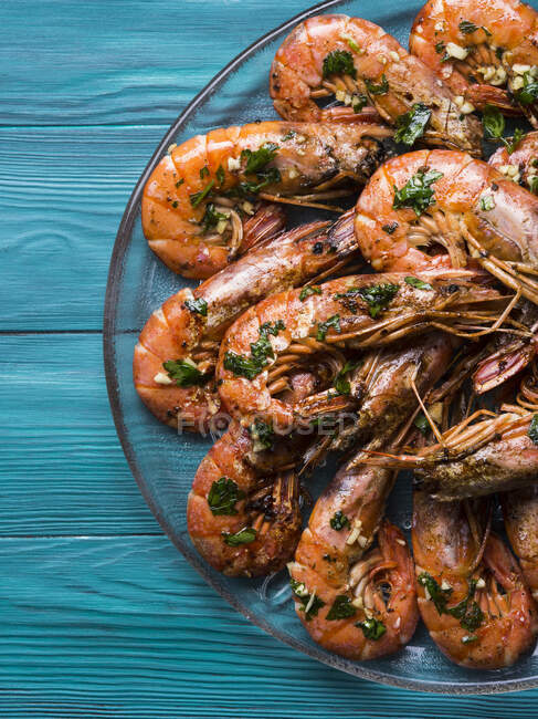 Grilled shrimps served on a dish with olive oil, parsley and garlic over dark green wooden background — Stock Photo