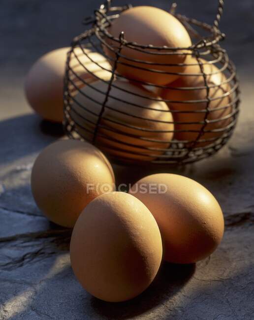 Uova fresche di fattoria su superficie di pietra e in mini cestino di filo — Foto stock